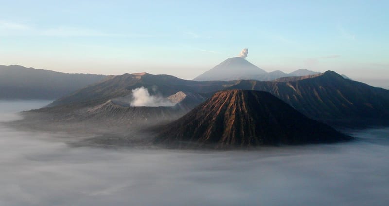 Kabut menyelimuti dasar kompleks Tengger; Bromo berkawah di kiri, Batok berbentuk kerucut di depan, Semeru di kejauhan.