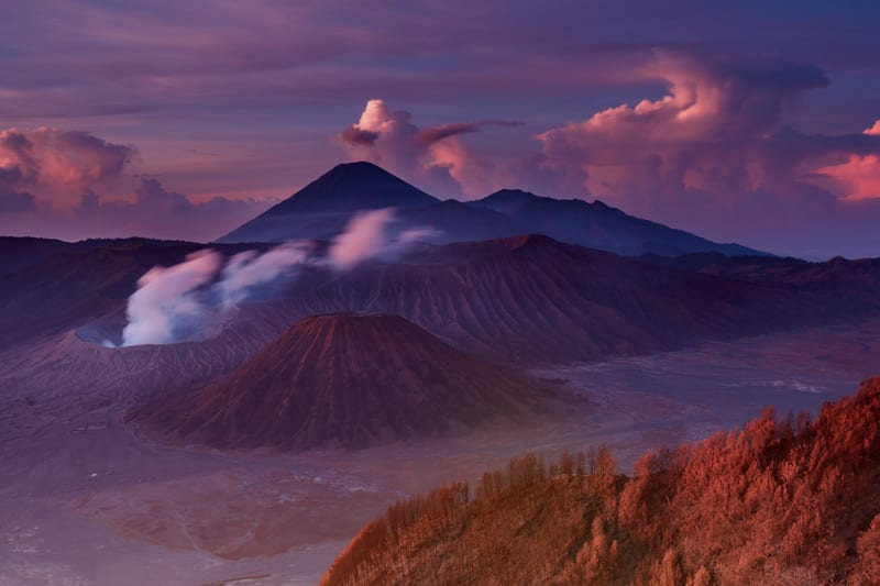 Kawah Bromo mengeluarkan asap di samping kerucut Batok dengan Semeru dan langit fajar di latar.